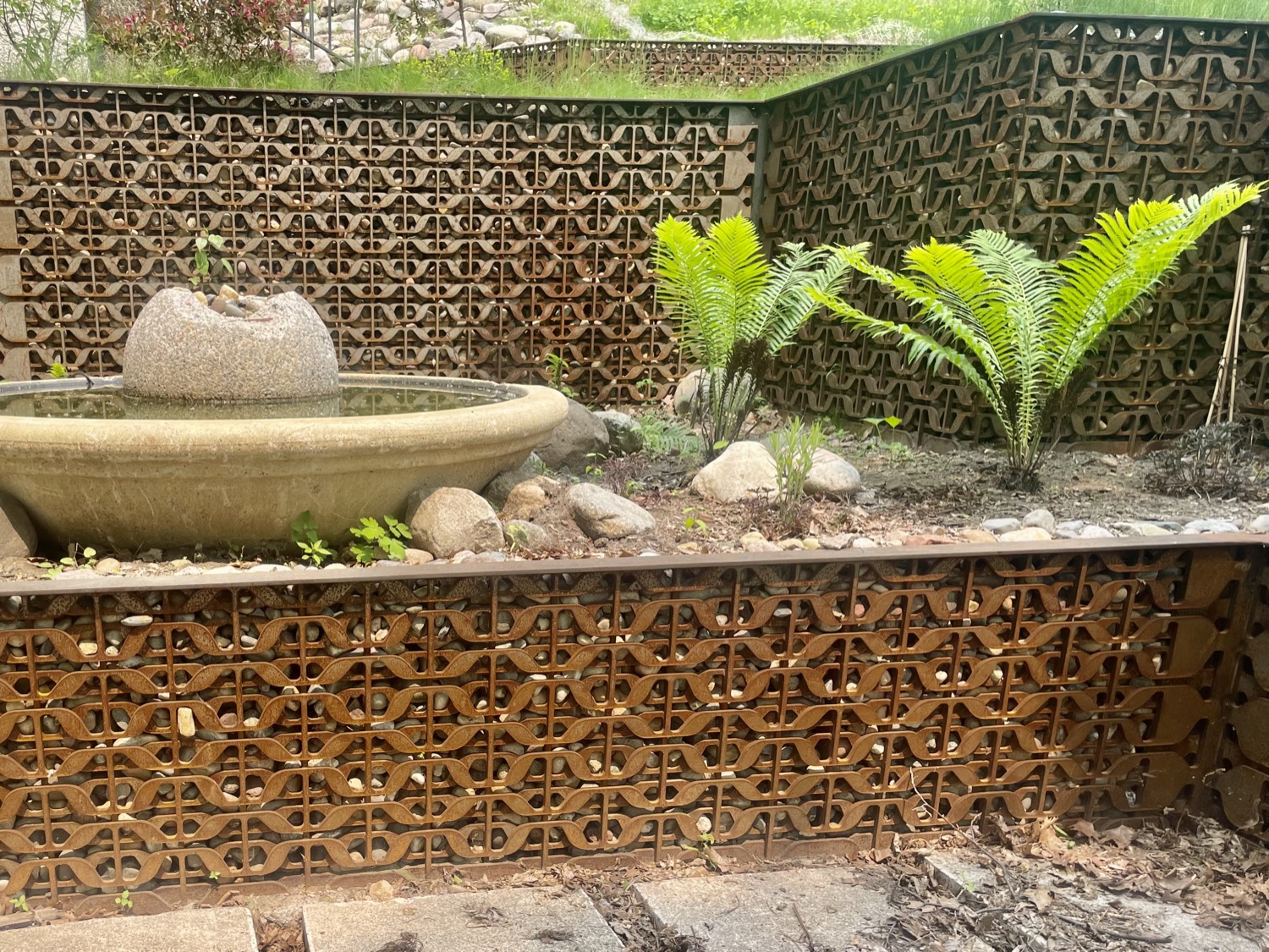 Stone water feature set into patterned gabion walls with ferns